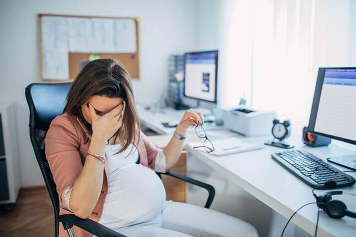Pregnant woman rubbing eyes at work - Pregnancy Discrimination
